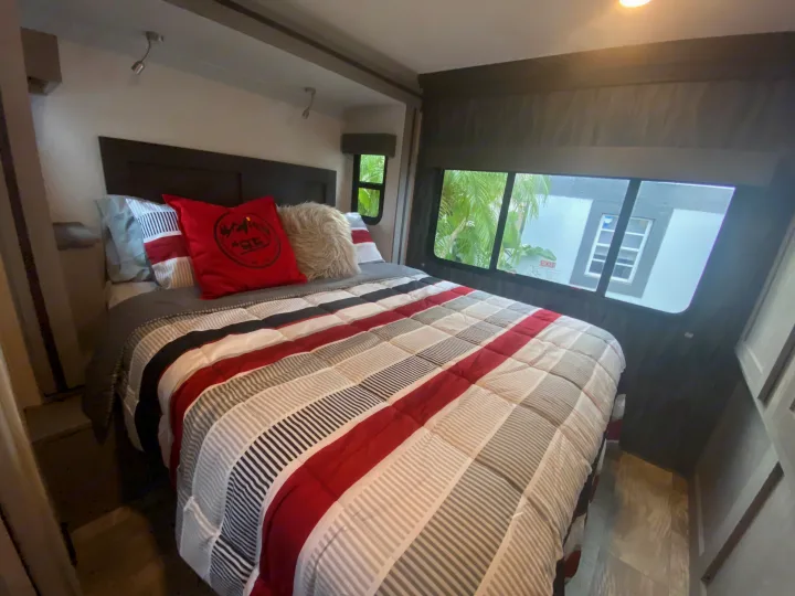 Comfortable RV rental bedroom featuring a striped bed, plush pillows, and scenic windows.. Forest River Solera 2022