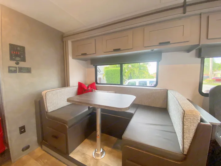This RV rental features a modern dinette with U-shaped seating, a table, and overhead cabinets, ideal for camper dining.. Forest River Solera 2022