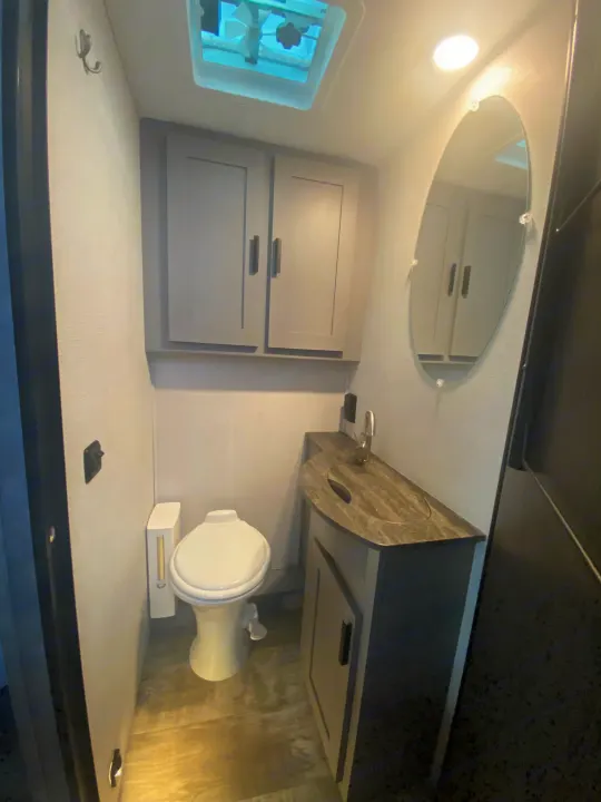 Compact RV rental bathroom featuring a toilet, functional vanity with sink, mirror, and overhead cabinets for convenience.. Forest River Solera 2022