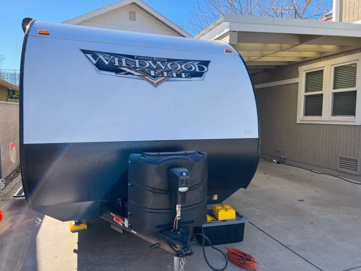 Front view of a Forest River Wildwood X-Lite travel trailer (RV), featuring propane tanks, jack, and leveling blocks. Perfect for rv rental.. Forest River Wildwood X-Lite 2021