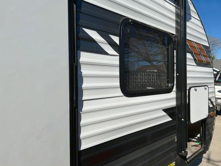 Close-up of an RV rental's side, featuring striped siding, a window, and an open storage compartment for gear.. Forest River Wildwood X-Lite 2021