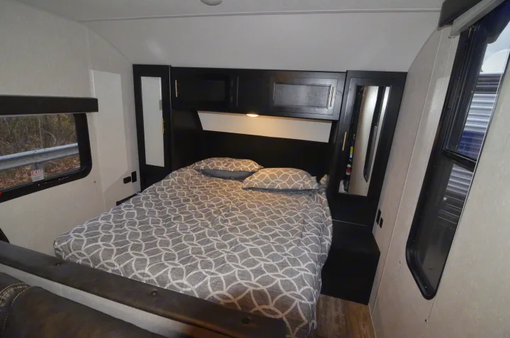 Comfortable RV rental bedroom with a patterned bed, dark built-in storage, and bright windows.. Forest River Cherokee 2021