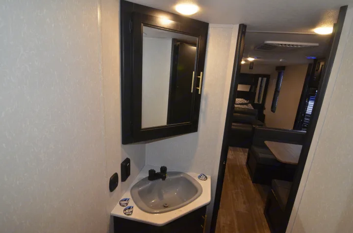 Compact RV interior featuring bathroom sink, mirror, and peek into the living space with dinette and bunks, ideal for your next rv rental.. Forest River Cherokee 2021
