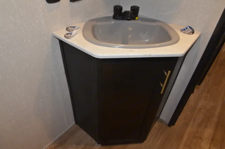 Compact corner sink vanity in a modern RV rental bathroom, featuring a gray basin, white counter, and dark cabinet.. Forest River Cherokee 2021