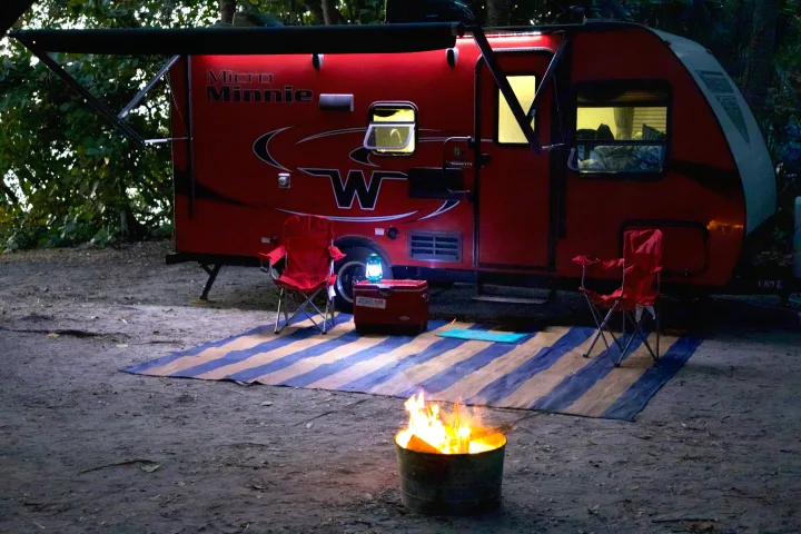Nighttime rv rental camp setup: a glowing fire, chairs, and illuminated red Micro Minnie trailer with awning.. Winnebago Micro Minnie 2018