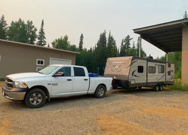 White pickup truck towing an RV rental travel trailer on gravel, ideal for camping and outdoor travel.. Keystone Hideout 2018