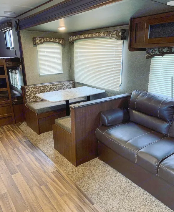 RV rental interior showcasing a booth dinette, dark sofa, wood-look flooring, and windows with blinds.. Keystone Hideout 2018
