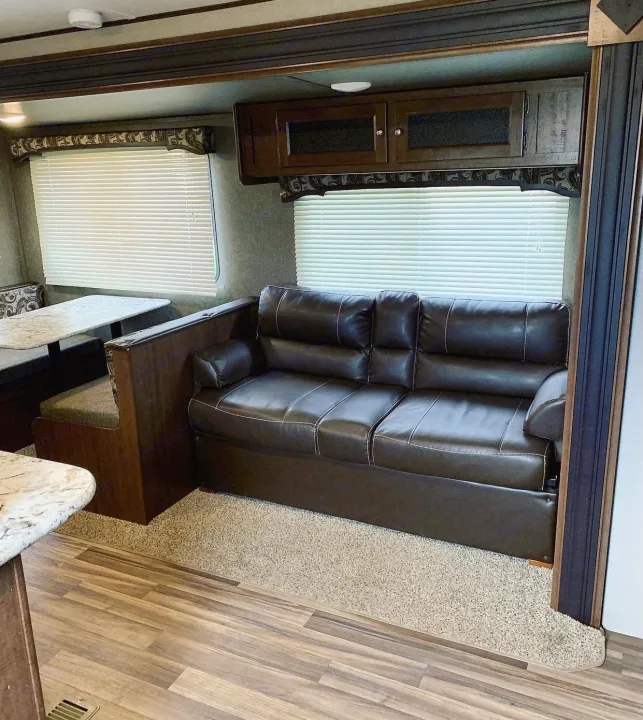 Spacious RV rental interior featuring a leather sofa, dinette, and overhead cabinets. Ideal for road trips.. Keystone Hideout 2018