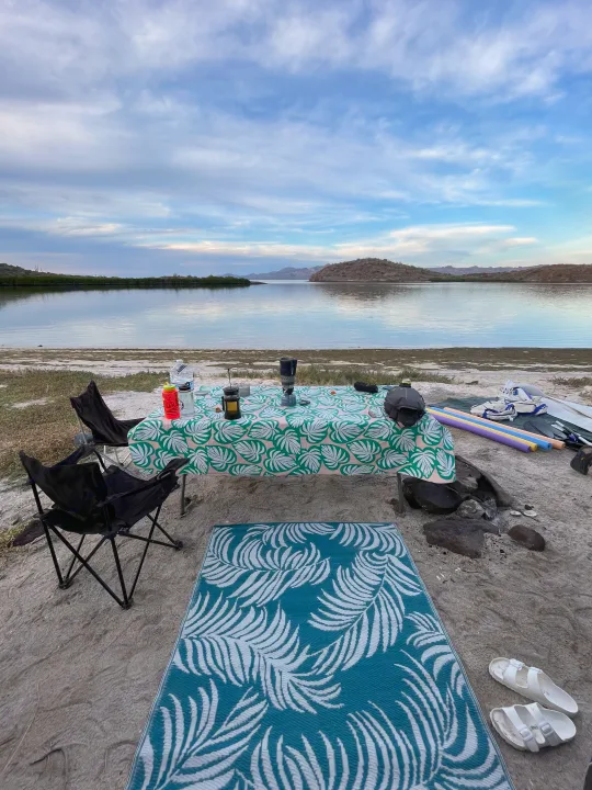 Relaxing lakeside camping setup, perfect for your RV rental trip! Features a table, chairs, mat, and stunning water views.. Ford Econolline 250s 2001