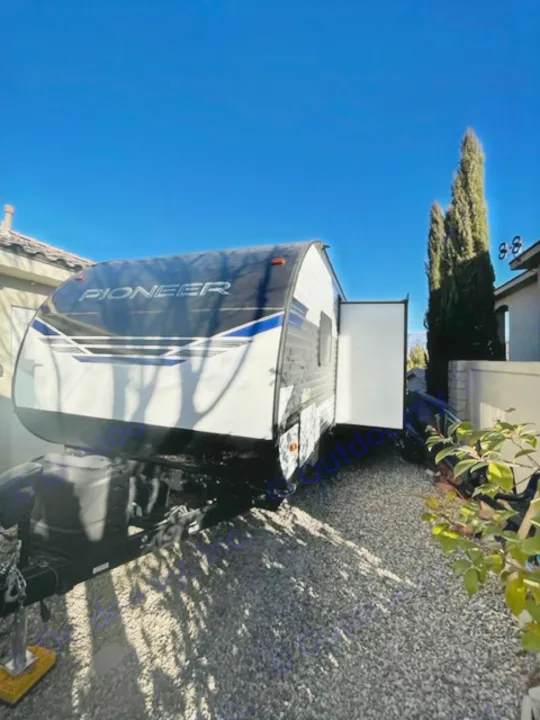 A white and black Pioneer travel trailer for RV rental, parked on gravel on a sunny day.. Heartland Pioneer 2021