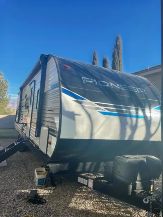 A sleek white and black Pioneer travel trailer, ideal for an RV rental, parked under a clear blue sky.. Heartland Pioneer 2021