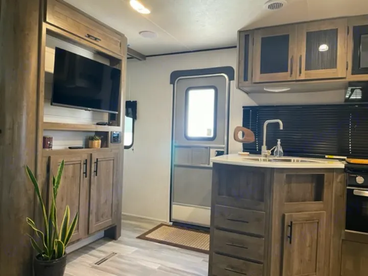 Tour a modern RV rental interior! View the light wood living area with TV, and kitchen with island sink & cabinets.. Heartland Pioneer 2021