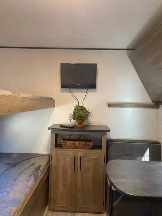 Modern RV rental interior with a wall-mounted TV, stylish wooden storage cabinet holding a plant and basket, and a comfy dinette.. Heartland Pioneer 2021