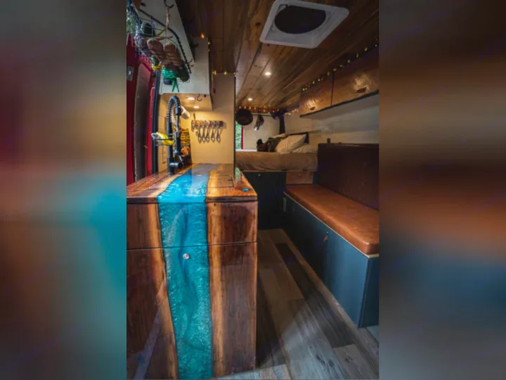 Inside a stylish custom RV rental: wood & blue resin kitchen, comfy bench seat, and bed. Perfect mobile living.. Dodge promaster 3500 2018