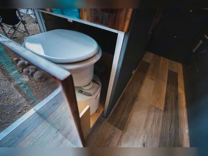 An open panel reveals a discreet composting toilet inside an RV rental, showing a compact, practical mobile bathroom solution.. Dodge promaster 3500 2018