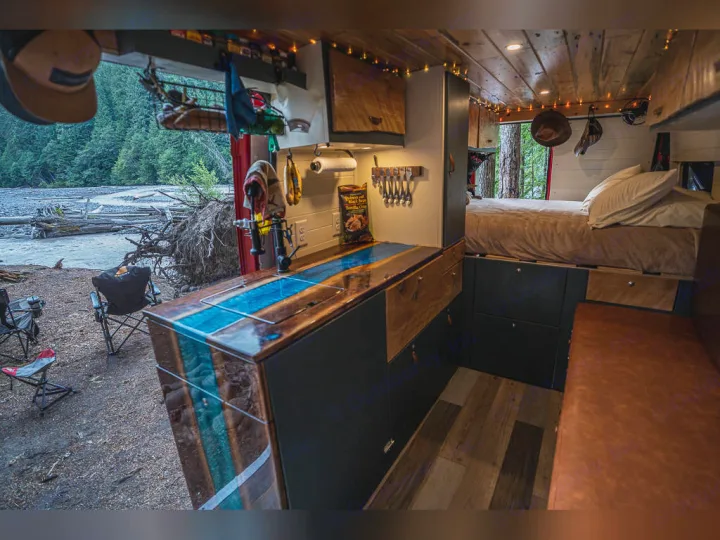 This RV rental shows a custom camper van's interior: kitchen with blue epoxy counter, bed, and a scenic river view outside.. Dodge promaster 3500 2018