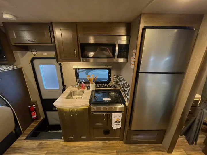 Inside an RV rental, this full kitchen features a stainless steel fridge, microwave, stove, and sink with ample cabinets.. Nexus Triumph 2022