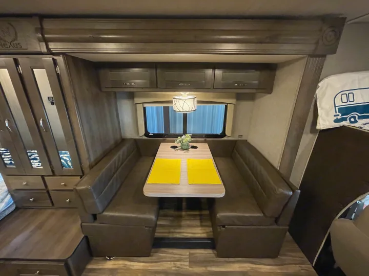 Spacious RV rental dinette with comfortable U-shaped seating, perfect for meals & relaxation. Features ample storage and bright lighting.. Nexus Triumph 2022