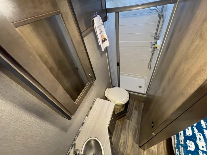 Compact and functional RV rental bathroom featuring a toilet, shower, and vanity with sink. Ideal for travel comfort.. Nexus Triumph 2022