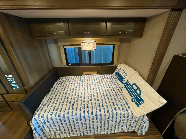 Cozy RV rental bedroom featuring a camper-themed bed, overhead storage, and a window, ideal for comfortable travels.. Nexus Triumph 2022