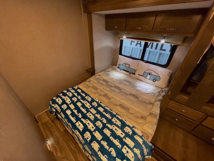 This cozy RV rental bedroom features a comfy bed with unique truck/camper pillows and an RV-themed blanket, plus useful overhead storage.. Nexus Triumph 2022
