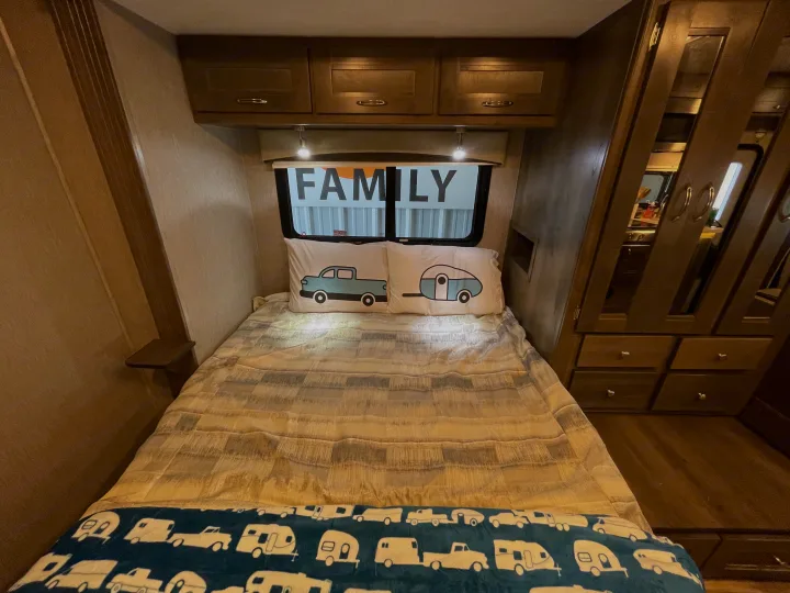 Cozy RV rental family bedroom: inviting bed with truck/camper pillows, overhead cabinets, and ample built-in storage.. Nexus Triumph 2022
