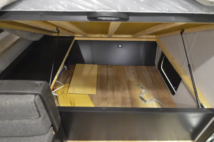 View of ample under-bed storage in an RV rental. Lifted mattress reveals a large, tidy compartment with wooden floor.. Forest River Cherokee 2021