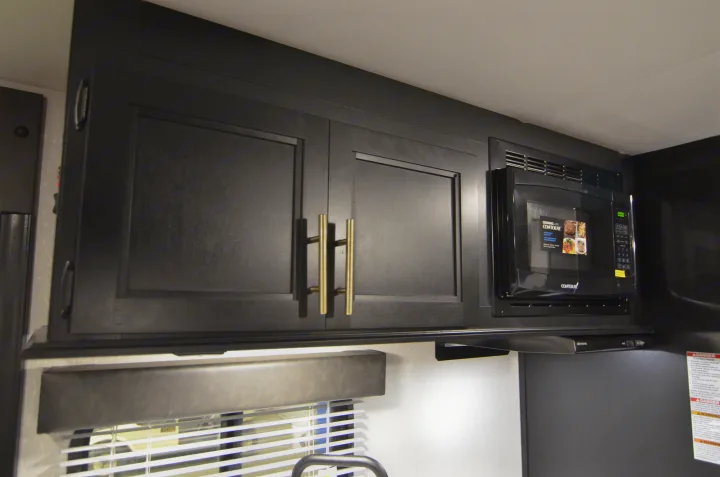 Modern RV rental kitchen featuring dark cabinets, gold handles, and an integrated microwave. Perfect for on-the-go cooking.. Forest River Cherokee 2021