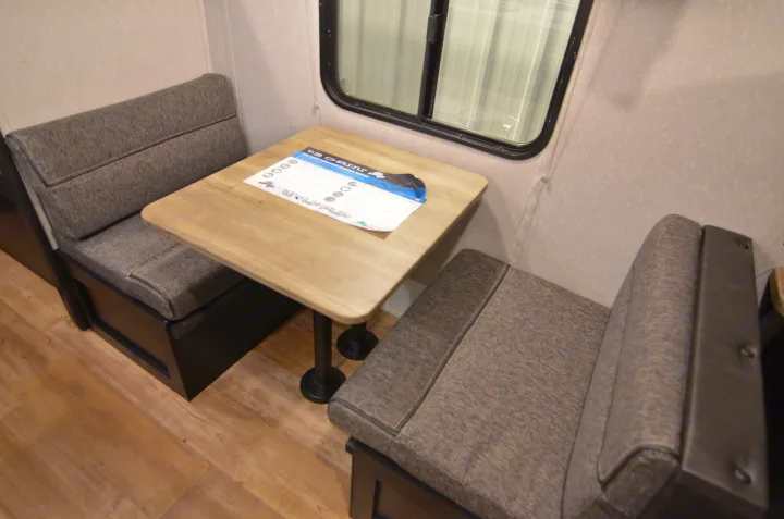 This RV rental interior shows a dinette with grey cushioned benches, a wood table, and a window for comfortable dining.. Forest River Cherokee 2021