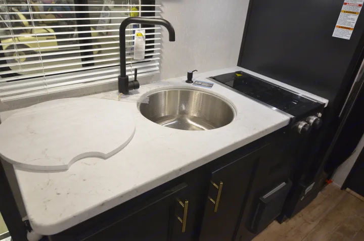 This RV rental features a compact kitchen with a light marble-look countertop, stainless sink, black faucet, and two-burner stovetop.. Forest River Cherokee 2021