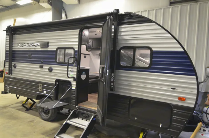 A modern grey and blue Wolf Pup travel trailer RV with its door open, showcasing the interior and an exterior awning, ready for RV rental.. Forest River Cherokee 2021