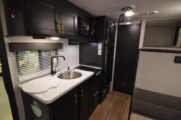 Compact RV rental interior featuring a modern kitchen with black cabinets, white counters, sink, stove, microwave, and bunk bed.. Forest River Cherokee 2021