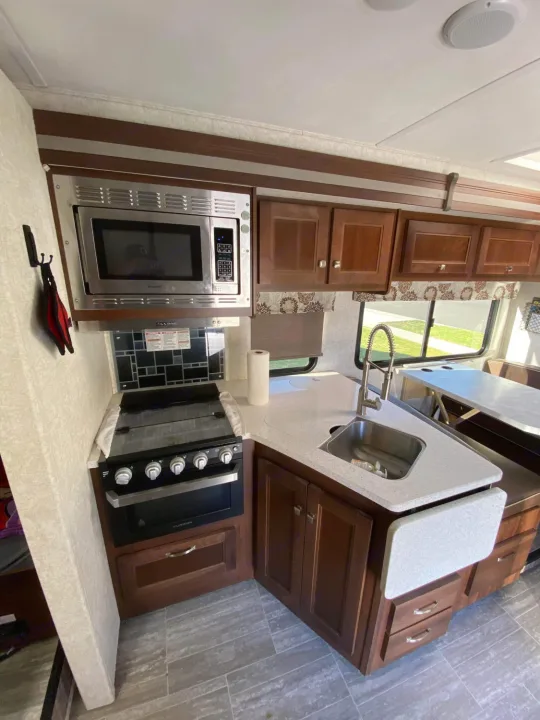 This RV rental kitchen features a microwave, stove, oven, sink, and ample cabinet space for cooking on the road.. Forest River Forester 2019