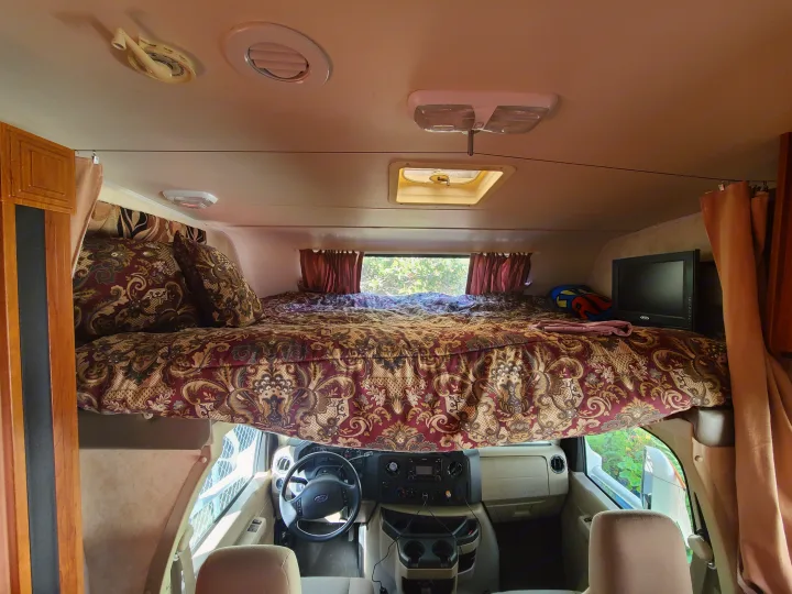 Interior view of an RV rental showing the spacious cab-over bed and front driver's cabin area. Relaxing travel.. Coachmen Freelander 2011