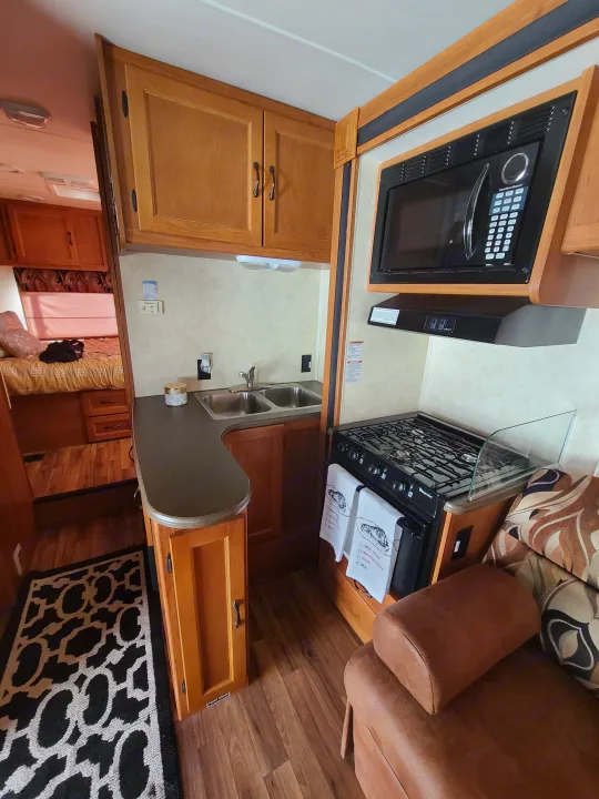 This RV rental features a compact kitchen with a sink, microwave, stove, and adjacent seating, perfect for travel.. Coachmen Freelander 2011
