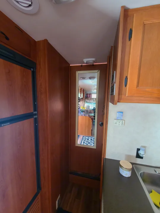 Inside an RV rental: View of the Dometic fridge, compact kitchen with sink, and hallway mirror reflecting the living area.. Coachmen Freelander 2011