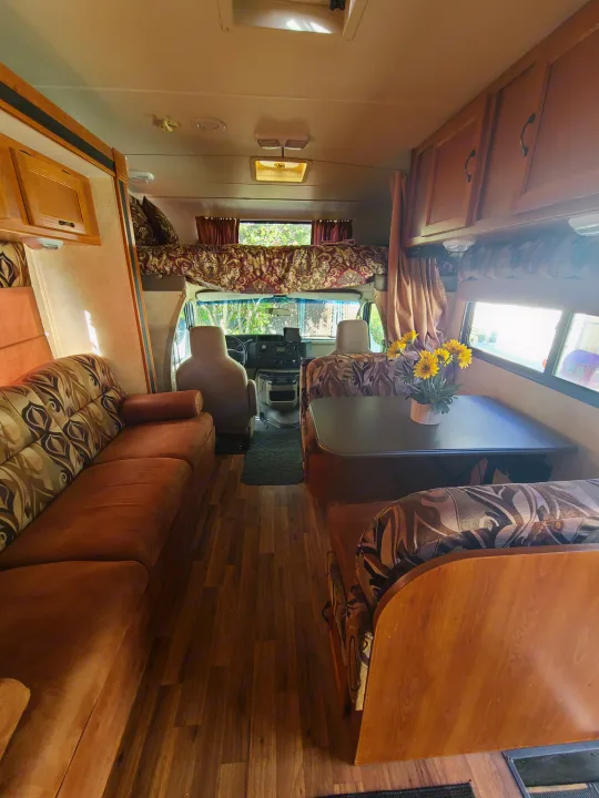 Cozy rv rental interior featuring a living room sofa, dining area, and cab-over bed. Perfect for your next adventure.. Coachmen Freelander 2011