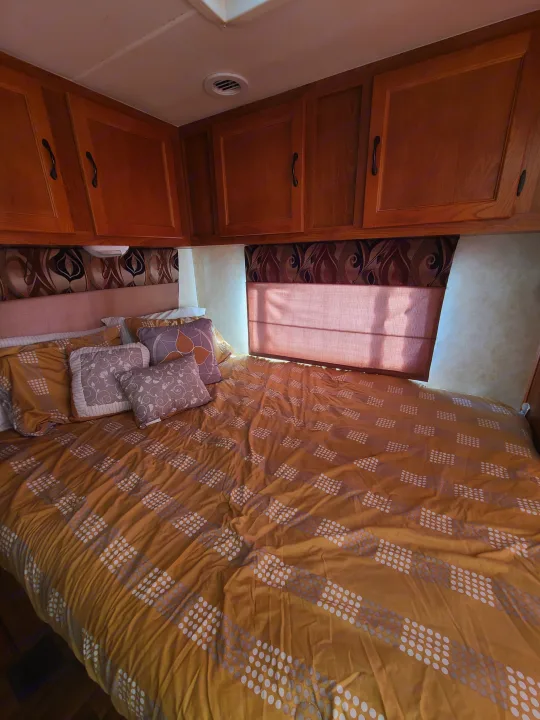 Cozy RV rental bedroom with patterned bedding, overhead cabinets, and a window, perfect for comfortable travel.. Coachmen Freelander 2011