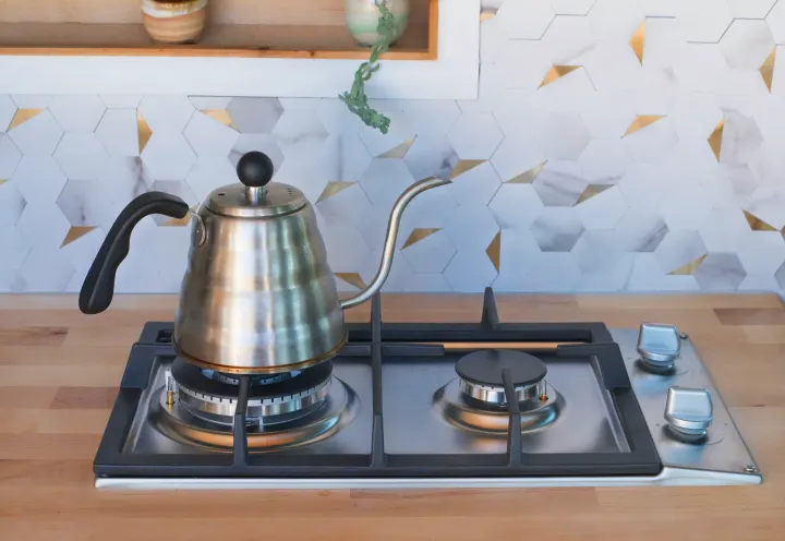 Clean RV rental kitchen with gooseneck kettle on gas stove, wood countertop, and modern hexagonal tile backsplash.. Mercedes-Benz Sprinter 2021