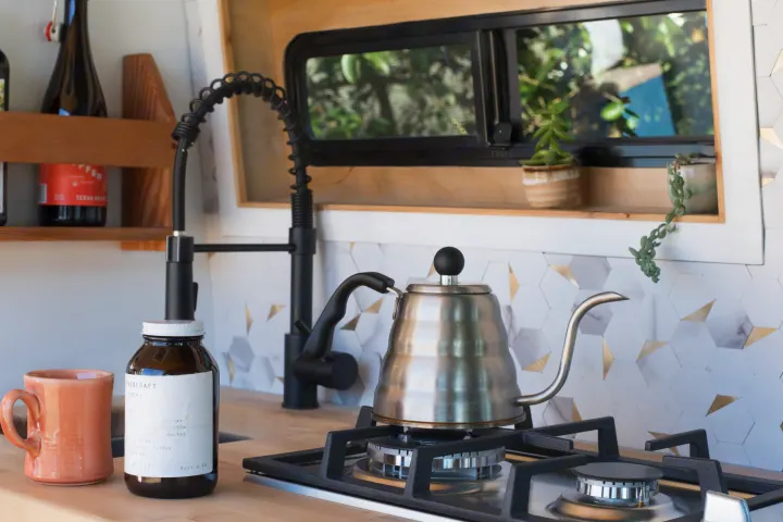 A modern RV rental kitchen features a sleek coffee setup: a gooseneck kettle on a gas stove next to a coffee jar and mug.. Mercedes-Benz Sprinter 2021