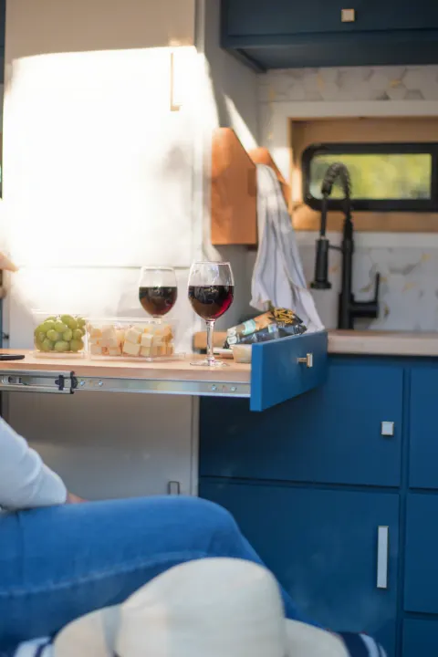 Wine, cheese, and grapes served on a pull-out table in a cozy RV rental with blue cabinets, great for travel.. Mercedes-Benz Sprinter 2021