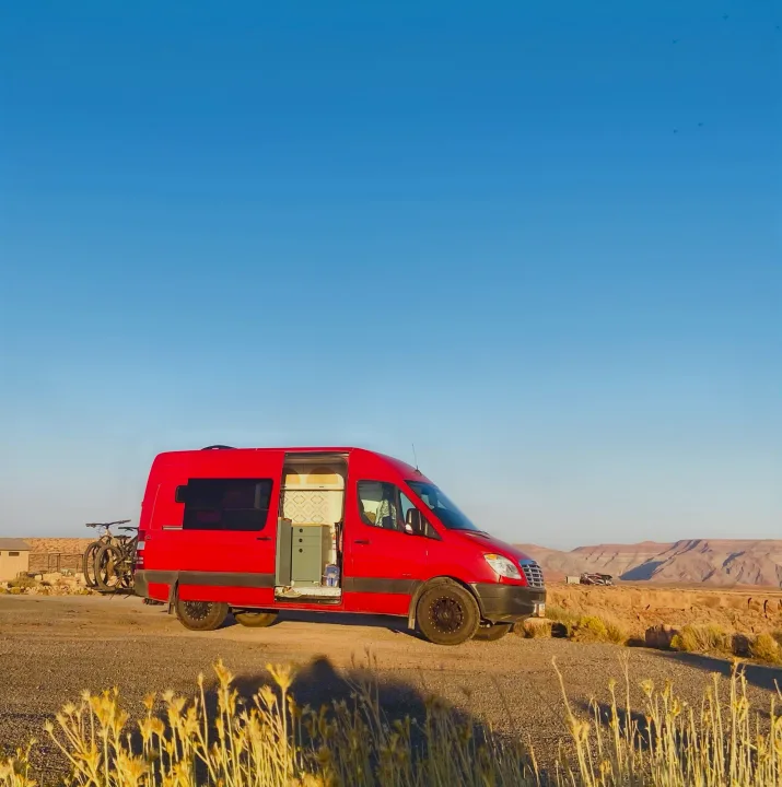 Bright red rv rental camper van, door open, with bikes on back, parked in a scenic desert mountain landscape. Enjoy van life!. Freightliner Sprinter 2011