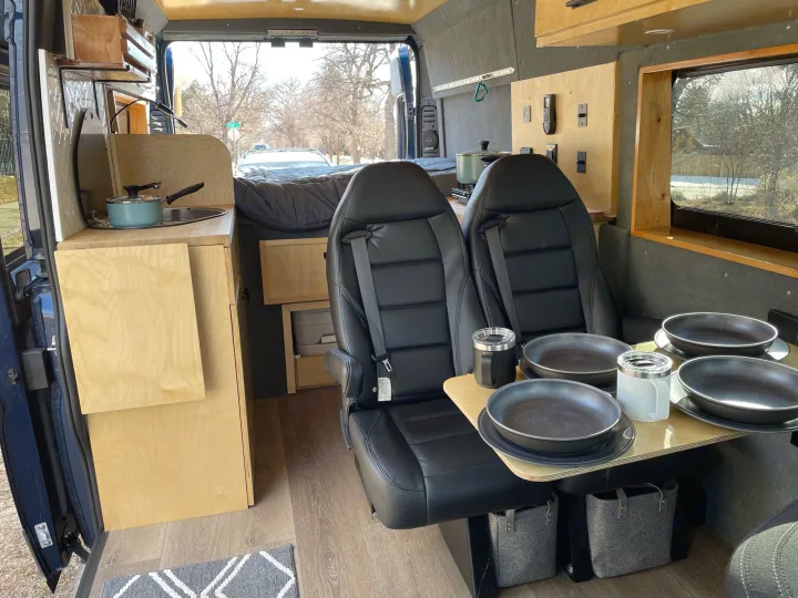 This RV rental features a functional camper van interior with kitchen, swivel seats, and rear bed setup.. Ram Promaster 2500 2021