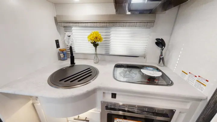RV rental kitchen: countertop with covered sink, stove, & microwave. Functional space for your travels.. Forest River R-Pod 2022