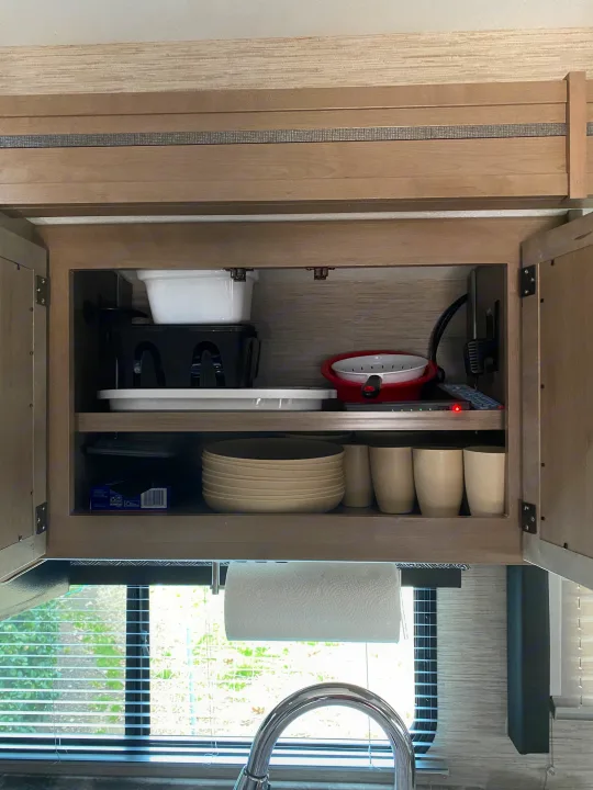 Kitchen cabinet in an **rv rental**, neatly stocked with dishes, cups, and a dish drainer.. Thor Magnitude 2022