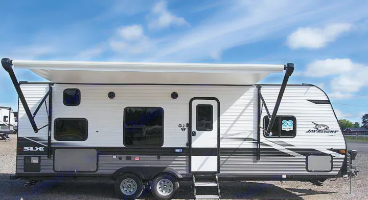 A white & grey Jay Flight SLX travel trailer, ideal for an RV rental, is parked with its awning extended under a blue sky.. Jayco Jay Flight 2022
