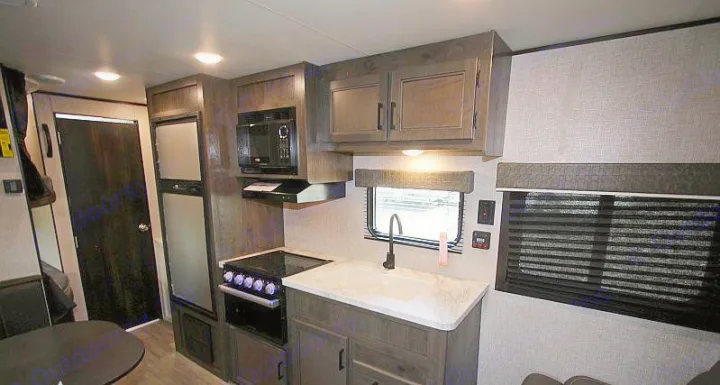 Inside an RV rental: modern kitchen with microwave, sink, stovetop, and fridge. Also shows a dining table and dark wood finishes.. Jayco Jay Flight 2022