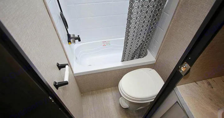 Compact RV rental bathroom with white toilet and small bathtub/shower combo featuring a patterned curtain. Ideal for travel.. Jayco Jay Flight 2022