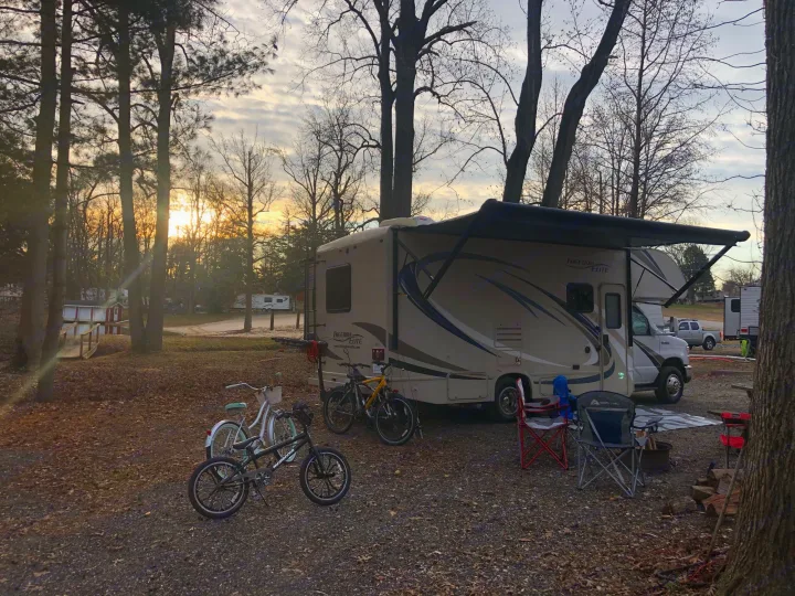 Enjoying a serene sunset at the campsite with our RV rental. Bikes, chairs, and a fire pit complete this peaceful outdoor leisure scene.. Thor Freedom Elite 2018