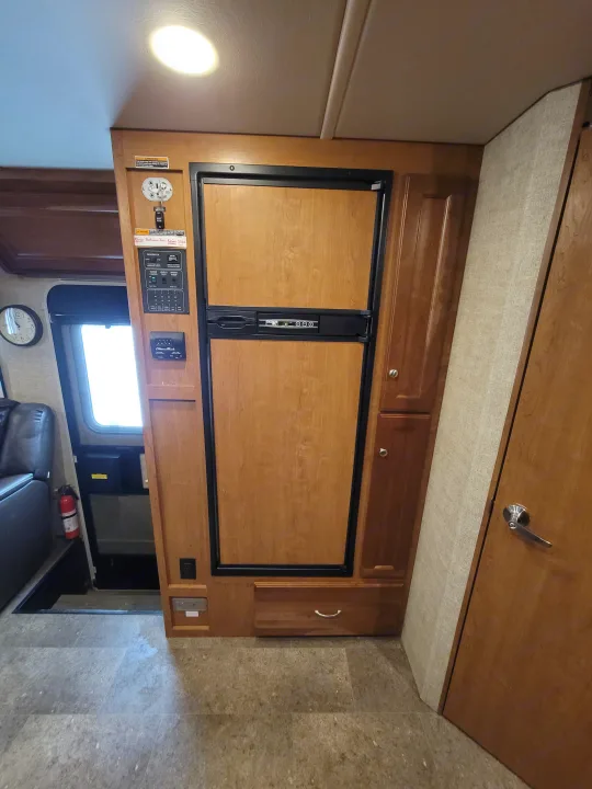 Interior of an RV rental, featuring a wood-paneled refrigerator, RV control panel, and overhead cabinets.. Winnebago Vista 2018